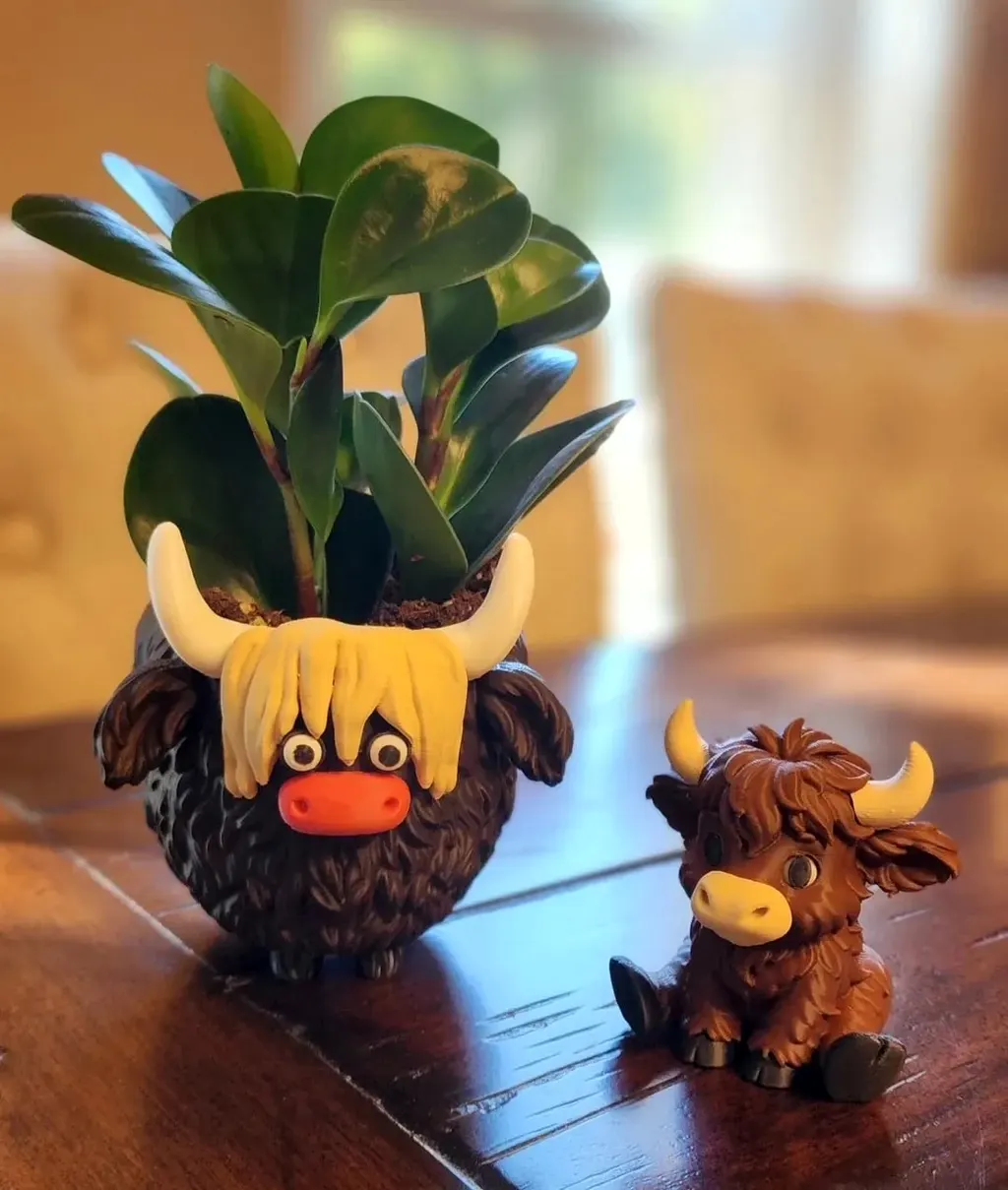Printed Highland cow planter holding a leafy houseplant, beside a small sitting Highland calf on a wooden table