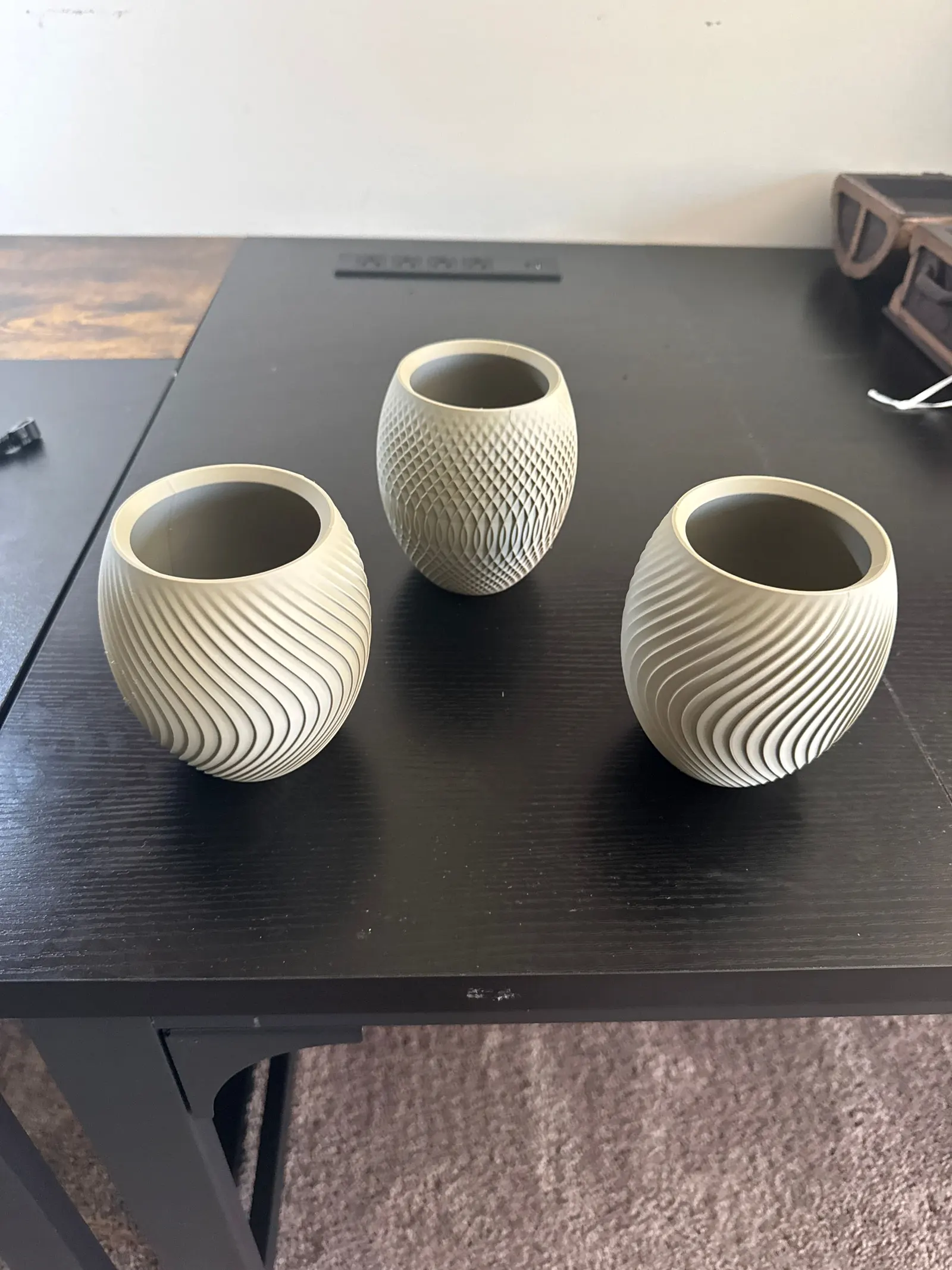 Three sand-colored vases with a textured surface on a black desk